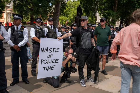 A protester in Londen holds his sign with text "Waste of Police Time" in front of a line of policemen at the Palestine Action demo.