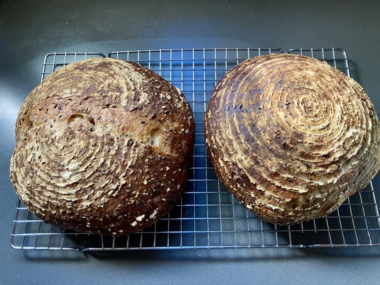 Two round loaves of freshly baked bread cooling on a wire rack. The crust is golden brown with a spiral pattern.