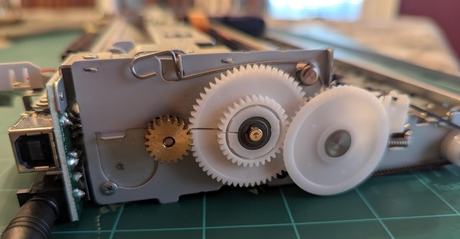 A shot of the printer with the case removed. There is a big white gear, between two others, that has a horizontal crack.