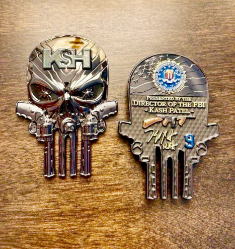 shiny gold objects in the shape of "The Punisher" skull with "KSH" on one side, and "DIRECTOR OF THE FBI KASH PATEL" over a rifle and signature on the other side. tackiest thing you can imagine.