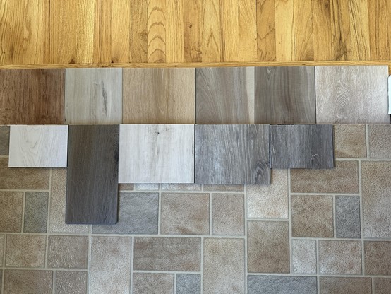 Flooring samples laid out between a bright orangey solid wood pecan hardwood floor, and vinyl sheet in beige and grey tones
