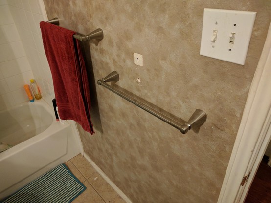 Two brushed metal towel rods on a light brown patterned bathroom wall. One has a fluffy red towel hanging over it. 

Multiple mounting holes from the single prior towel bar are unrepaired and highly visible because I didn't want to attempt the custom light brown pattern at the time.